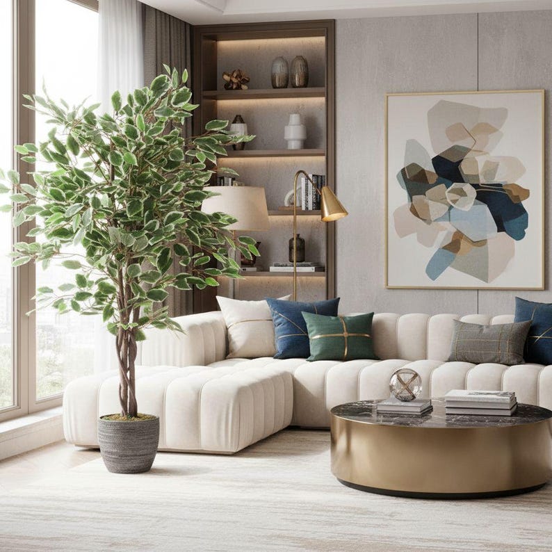 May include: A modern living room featuring a large, cream-colored sectional sofa with decorative pillows in shades of blue and green. A round gold coffee table sits in front of the sofa, and a large abstract painting hangs on the wall. A tall potted plant adds a touch of nature.