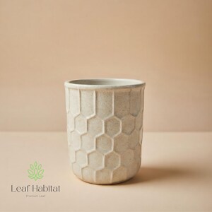 May include: A beige ceramic plant pot with a honeycomb design. The cylindrical pot has a textured surface and a wide, smooth rim. The pot is suitable for indoor or outdoor use.