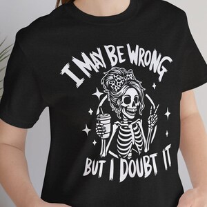 May include: Black t-shirt with a white graphic of a skeleton with a bow, holding a coffee cup and giving a thumbs up. The text reads "I MAY BE WRONG BUT I DOUBT IT".