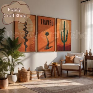May include: Three framed art prints with desert landscape designs in orange, brown, and green hues. The middle print features the word "TRAVEL" in bold letters. The prints are displayed above a white armchair and a wooden side table, creating a warm, inviting atmosphere.