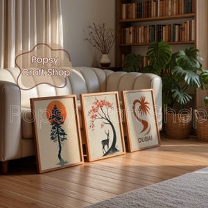 May include: Three framed art prints with nature-themed illustrations. One features a tree silhouette against an orange sun, another a deer under a cherry blossom tree, and the third a palm tree design with the word "DUBAI".