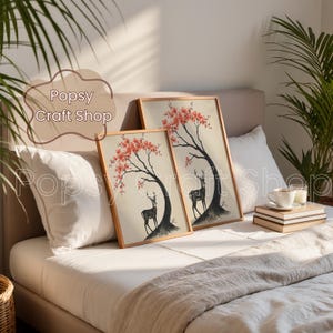 May include: Two framed art prints featuring a black deer under a tree with red blossoms. The prints are displayed on a bed with white pillows and a beige blanket. The text "Popsy Craft Shop" is visible in the image.