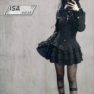 May include: A black dress with a layered skirt and long sleeves. The dress has button details and ruffled accents. The image includes the text "ISABEL STREETWEAR" in a white and black logo.