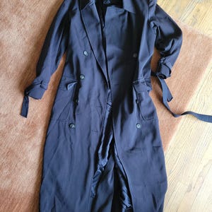 May include: A long black trench coat with a double breasted closure, a belt, and pockets.