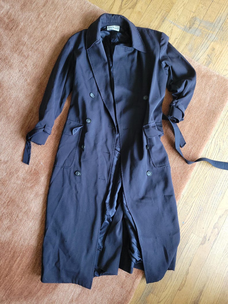May include: A long black trench coat with a double breasted closure, a belt, and pockets.