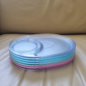 Könnte beinhalten: Ein Stapel aus sechs durchsichtigen Plastiktabletts mit einem erhöhten Ring in der Mitte. Die Tabletts sind durchscheinend und haben einen leichten irisierenden Schimmer. Die Tabletts sind nach Farbe sortiert gestapelt, beginnend mit dem hellsten Blau oben und endend mit dem dunkelsten Lila unten. Die Tabletts sind alle gleich groß und gleich geformt.