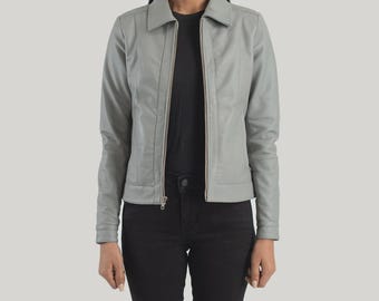 May include: A pale grey leather jacket featuring a collared neckline and a full-length zip. The jacket has long sleeves and a tailored fit. The model is wearing black trousers and a black top.