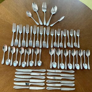 May include: A collection of silver-colored flatware, including forks, spoons, and knives, arranged on a wooden surface. The silverware is displayed in neat rows, showcasing a classic design suitable for formal dining.