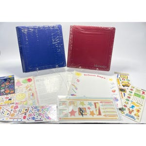 Könnte beinhalten: Eine Sammlung von Scrapbooking-Zubehör, darunter ein blaues und ein rotes Album, Aufkleber und dekoratives Papier. Die Alben sind in Plastik verpackt. Die Aufkleber zeigen Designs zum Thema Schule und andere farbenfrohe Grafiken.