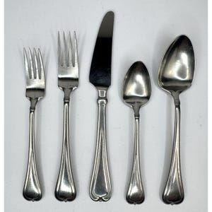 Könnte beinhalten: Ein Set aus fünf silberfarbenen Besteckteilen: zwei Gabeln, ein Messer und zwei Löffel. Das Besteck hat ein klassisches Design mit einem dekorativen Griff. Die Messerklinge ist glatt und die Löffel haben eine abgerundete Schalenform. Das Besteck ist auf einer weißen Oberfläche angeordnet.