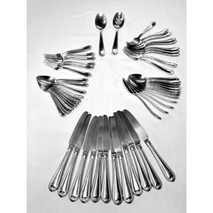 May include: Arrangement of silverware including spoons, forks, and knives. The silverware is made of a shiny, silver-colored metal. The knives have a decorative handle design. The forks, spoons, and knives are arranged in a fan-like pattern.