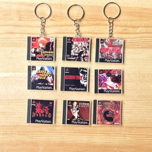 May include: A collection of nine PlayStation game keyrings, including titles such as Castlevania and Tomb Raider. Each keyring displays a game cover design and the PlayStation logo, attached to a silver chain and ring.
