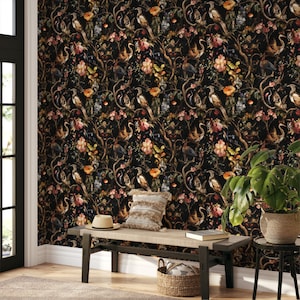 May include: A room with a black floral wallpaper featuring birds, flowers, and branches. A bench with a hat and pillow sits in front of the wall. A potted plant and a small table are also in the room. The wallpaper has a dark, moody aesthetic.