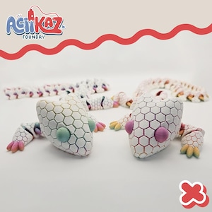May include: White articulated lizard toys with a honeycomb pattern. The lizards have colorful accents on their feet and eyes. The image includes the "AciiKaz Foundry" logo in the upper left corner.