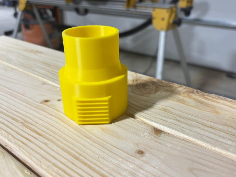 Puede incluir: Un adaptador de pl&aacute;stico amarillo brillante con una parte superior cil&iacute;ndrica y una base hexagonal con ranuras horizontales. Dise&ntilde;ado para conectar componentes, descansa sobre una superficie de madera clara.