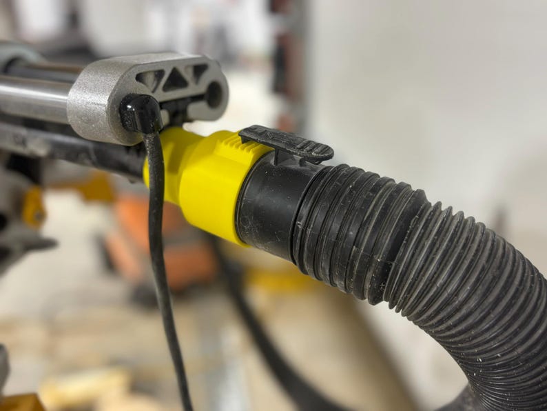 Puede incluir: Primer plano de una herramienta el&eacute;ctrica con una manguera negra corrugada conectada a un conector amarillo y negro. Un cable negro se extiende desde la herramienta. La herramienta tiene una carcasa de metal plateado.