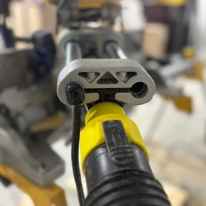 Puede incluir: Primer plano de una sierra ingletadora gris y amarilla. La sierra tiene una carcasa de metal gris con un cable de alimentaci&oacute;n negro y un conector amarillo. La sierra est&aacute; dise&ntilde;ada para cortar madera y otros materiales.