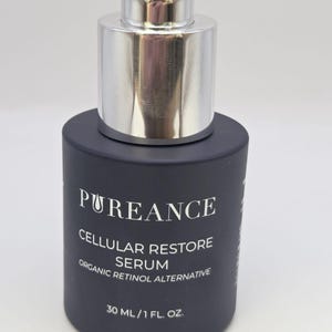 May include: A dark blue serum bottle with a silver cap. The bottle has white text that reads "PUREANCE CELLULAR RESTORE SERUM ORGANIC RETINOL ALTERNATIVE" and "30 ML/1 FL. OZ."
