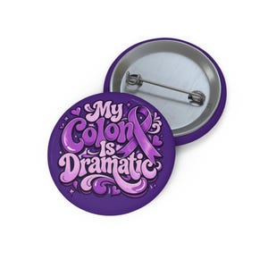 May include: Two purple round buttons. One button features the text "My Colon is Dramatic" in a stylized font, with a purple ribbon graphic. The other button is silver and purple.