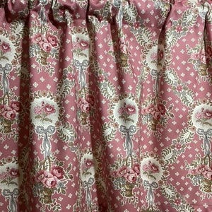 Può includere: Una tendina a balza arricciata con un motivo floreale. Il tessuto è di colore rosa antico con un motivo ripetuto di bouquet floreali, nastri e piccoli fiori bianchi. La tendina è arricciata nella parte superiore.