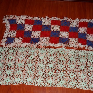 May include: Two crocheted table runners. The top runner is white with red, blue, and white squares. The bottom runner is a light green colour.