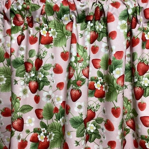 Puede incluir: Cortina de tela rosa con un estampado repetido de fresas rojas, hojas verdes y flores blancas. La cortina tiene una parte superior fruncida y un fondo rosa claro. El diseño es un estampado botánico.