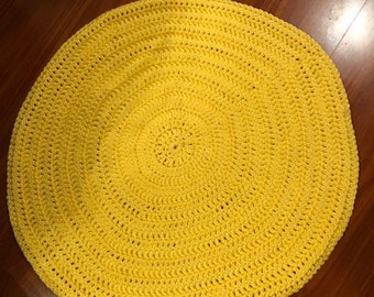 May include: A round, yellow crocheted rug with a circular pattern. The rug is made of thick yarn and has a soft, textured surface.