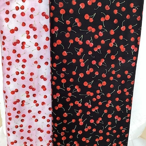 Peut inclure: Deux rouleaux de tissu, un rose clair et un noir, tous deux ornés de motifs de cerises rouges. Les cerises ont des tiges vertes et sont dispersées sur le tissu. Le tissu est probablement du coton ou une matière similaire, adapté aux projets de couture.