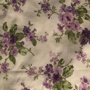 May include: A white fabric with a repeating pattern of purple flowers and green leaves.