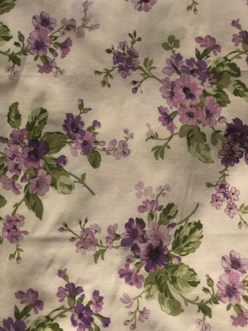 May include: A white fabric with a repeating pattern of purple flowers and green leaves.