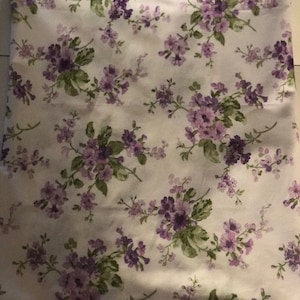 May include: White fabric with a repeating pattern of small purple flowers and green leaves.