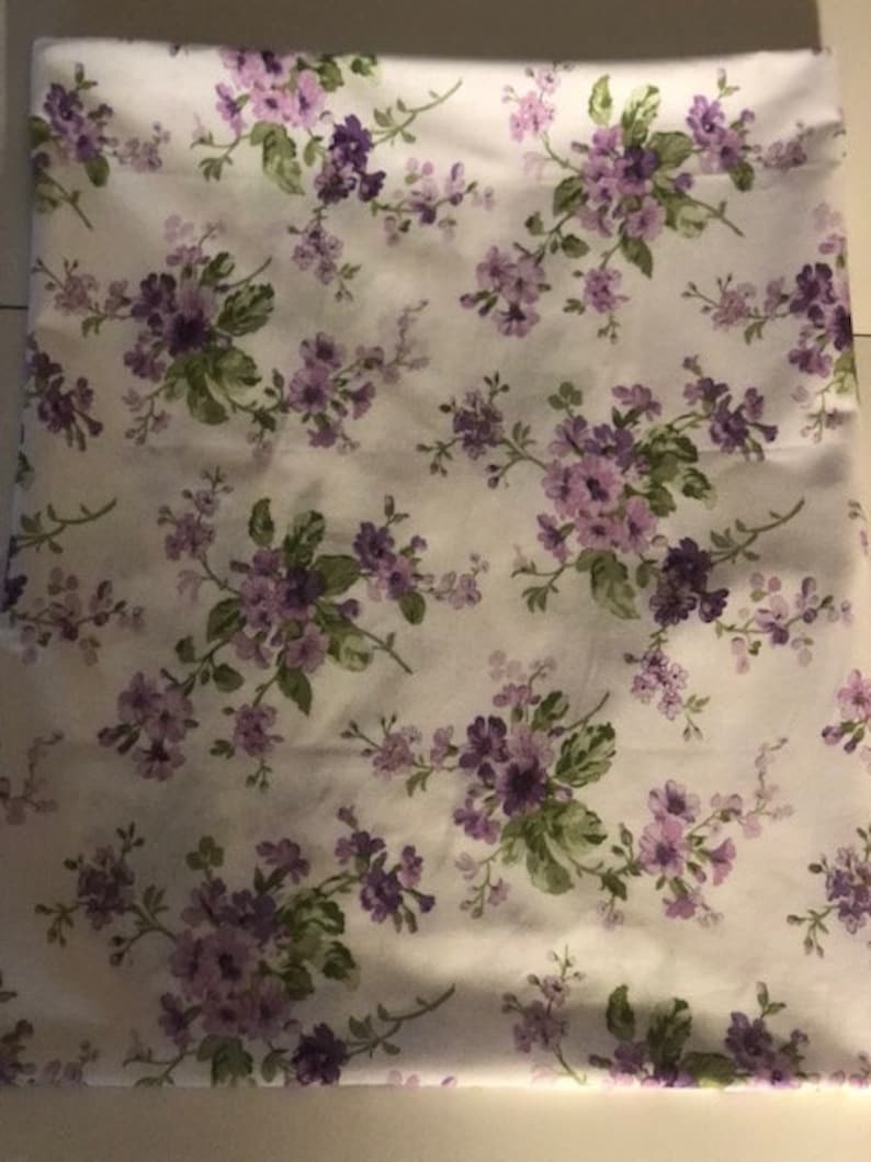 May include: White fabric with a repeating pattern of small purple flowers and green leaves.