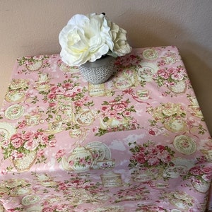 Peut inclure: Une nappe rose à motif floral avec des tasses à thé, des théières et des roses. Un arrangement de fleurs blanches est dans un pot gris sur la nappe.
