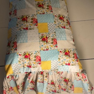 May include: A patchwork pillow with a ruffled edge. The pillow is made of a variety of fabrics in shades of blue, yellow, and white, with a floral pattern.