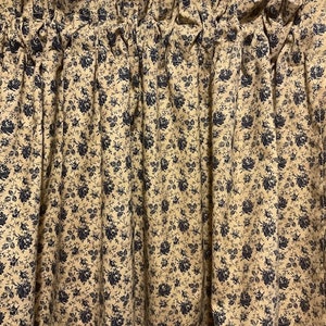 Può includere: Una tenda a valance con sfondo crema e un piccolo motivo floreale blu. La tenda ha un aspetto arricciato ed è realizzata in un tessuto morbido.