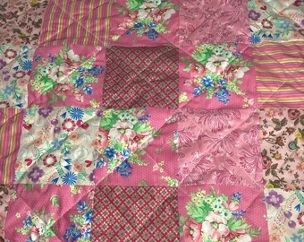 May include: A patchwork quilt featuring a variety of pink floral and patterned fabrics. The quilt is composed of square blocks, each with a different design, including floral prints, stripes, and geometric patterns. The quilt is quilted with a diamond pattern.