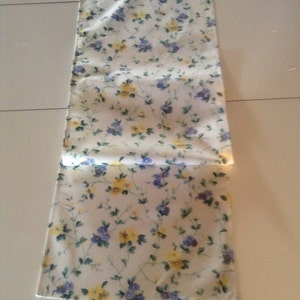 Könnte beinhalten: Ein weißer Tischläufer mit einem floralen Muster mit gelben und blauen Blumen auf weißem Hintergrund.