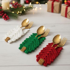 Puede incluir: Tres soportes para utensilios con forma de árbol de Navidad de ganchillo en blanco, verde y rojo, cada uno con una cuchara y un tenedor dorados. Los soportes tienen un detalle de tronco de ganchillo marrón. Decoración festiva navideña.