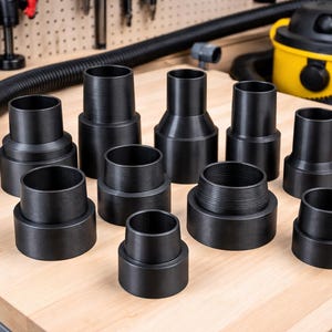 May include: A collection of black vacuum cleaner attachments of various sizes and shapes, arranged on a light wood surface. The attachments include hose connectors and adapters, designed for different vacuuming needs. A yellow and black vacuum cleaner is visible in the background.
