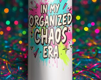 以下が含まれることがあります： カラフルなスプラッシュペイントデザインの「IN MY ORGANIZED CHAOS ERA」というテキストが入った白いタンブラー。デザインにはピンク、ティール、イエローのアクセントが含まれています。タンブラーは円筒形で、金属製のように見えます。