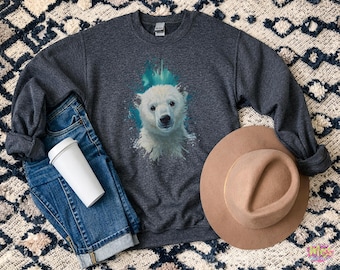 以下が含まれることがあります： ターコイズのアクセントが付いたホッキョクグマのグラフィックが特徴の濃い灰色のスウェットシャツ。画像には、青いジーンズ、白いコーヒーカップ、茶色のフェドラハットが含まれています。スウェットシャツはクルーネックです。