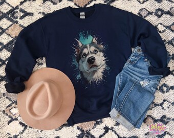 以下が含まれることがあります： ネイビーブルーのスウェットシャツ。青い目をしたハスキー犬のイラストと、ターコイズと白のペイントスプラッシュが特徴です。青いジーンズとベージュのフェドラハットも写っています。