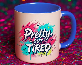 以下が含まれることがあります： 青いハンドルと内側を備えたクリーム色のセラミックマグ。マグには、カラフルなグラフィティスタイルのデザインで「Pretty but Tired」という言葉が書かれています。マグは光沢のある仕上がりです。