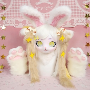 Puede incluir: Un disfraz de conejito blanco con orejas grandes, interior rosa y pelo largo y fluido. La m&aacute;scara tiene ojos amarillos grandes y una peque&ntilde;a nariz rosa. Incluye manoplas a juego con forma de pata y estrellas decorativas.