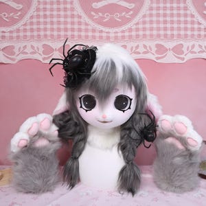 May include: A white and gray bunny-themed costume head with large, expressive eyes and long, gray braids. The costume includes large, fluffy gray paw-shaped gloves with pink pads and a black spider hair accessory.