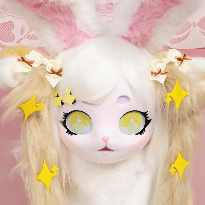 Puede incluir: Una m&aacute;scara de conejo blanca y rosa con grandes ojos amarillos y detalles de estrellas. La m&aacute;scara tiene pelaje blanco esponjoso, orejas largas y peque&ntilde;os lazos. El dise&ntilde;o es caprichoso y lindo, con un enfoque en el personaje del conejo.