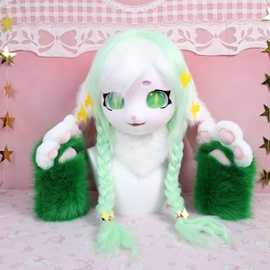 May include: A white and green furry fursuit head with matching green braids and paw-shaped hand covers. The head has large green eyes, star accents, and a white fur chest. The hand covers are green with white paw pads.