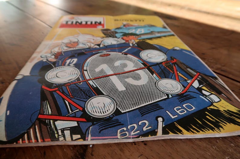 May include: A vintage comic book cover featuring a blue race car with the number 13 prominently displayed on its front grille. The illustration includes the text TINTIN in a red box at the top, along with the license plate number 622 L60.