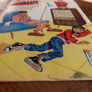 May include: A vintage magazine cover featuring a colorful illustration of a person in a red sweater and blue jeans lying on a yellow floor, with a television set and a person in a blue chair in the background. The text reads TV PROGRAMME CE SOIR LES AVENTURES DE TINTIN ET MILOU.