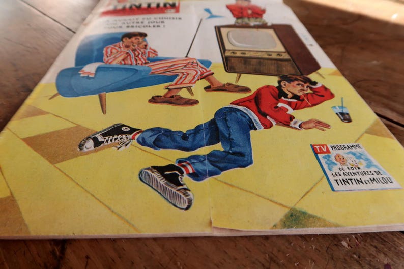 May include: A vintage magazine cover featuring a colorful illustration of a person in a red sweater and blue jeans lying on a yellow floor, with a television set and a person in a blue chair in the background. The text reads TV PROGRAMME CE SOIR LES AVENTURES DE TINTIN ET MILOU.